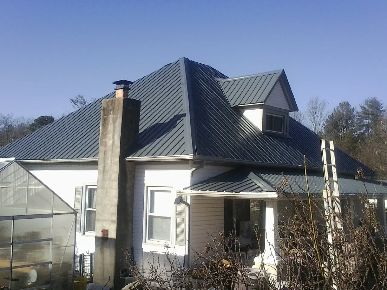 Dark blue standing seam metal roof on a white farmhouse with dormer — Slate & Tile Roof Repair by Roofing Brothers in Bonneau