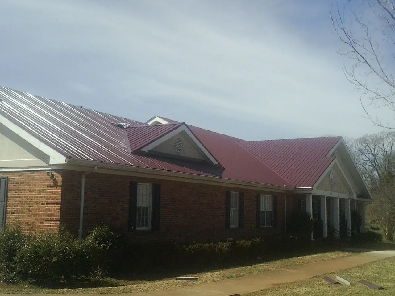Red metal roof with gabled entries on a long brick building, from a Hail Damage Roof Repair job in Bonneau