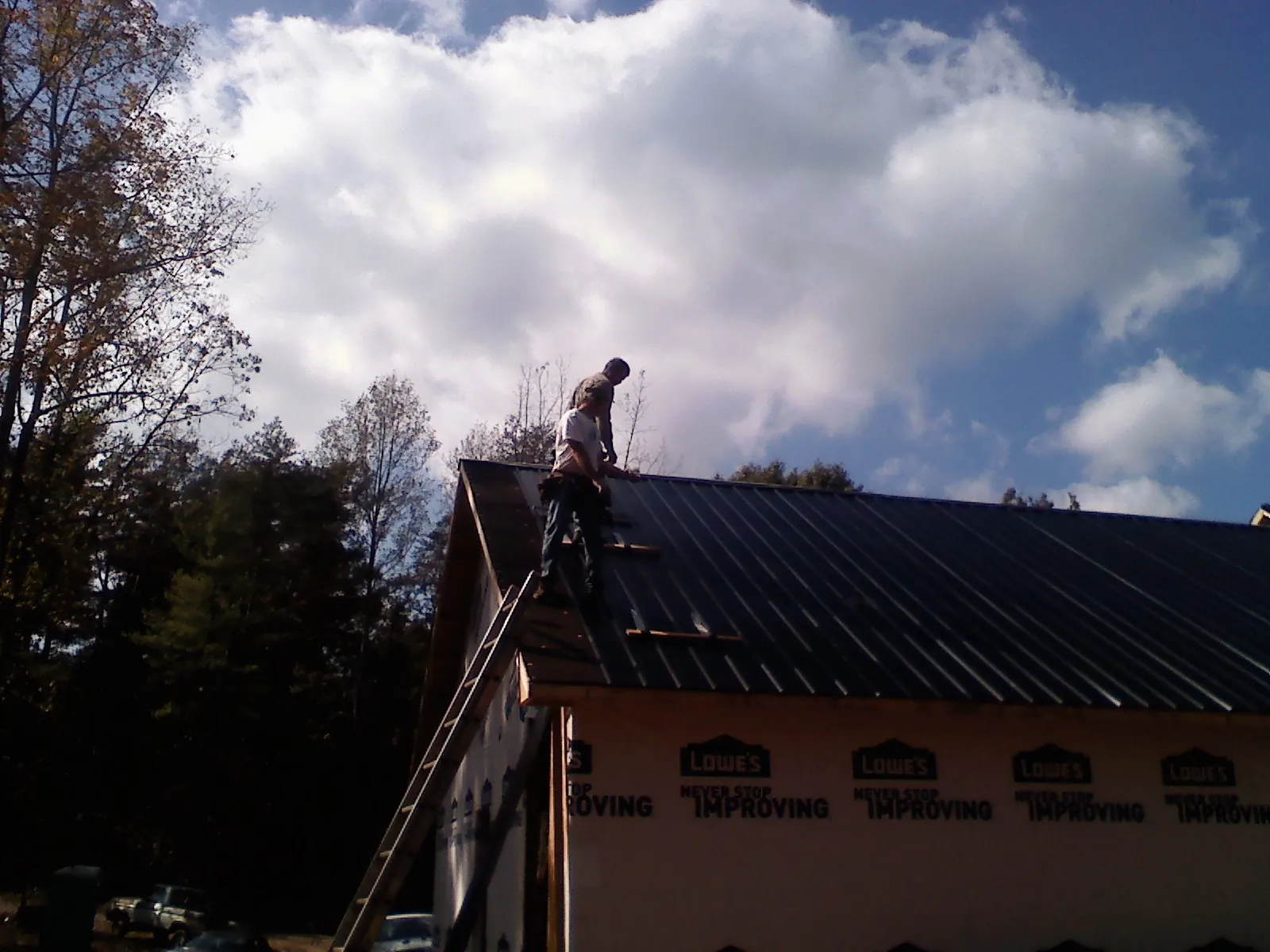 Roofer fastening dark metal panels high against a cloudy sky, from a Roof Inspection job in Bonneau